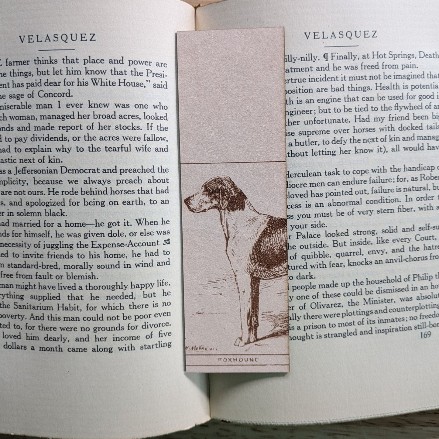 A rectangular leather bookmark with the historical art of a foxhound dog engraved on it. The bookmark is resting on the pages of an open book. Leather Foxhound Bookmark Bookmarks Raven King Crafts Leather Foxhound Bookmark Bookmarks Raven King Crafts
