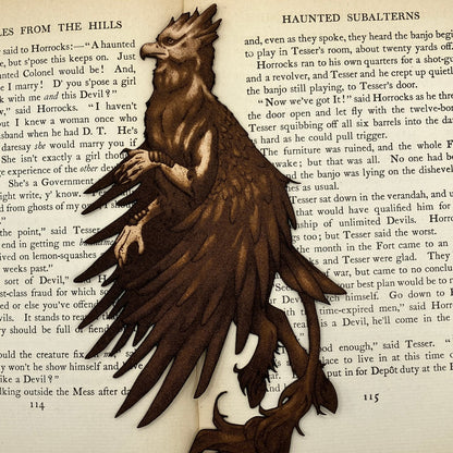 A leather hippogriff bookmark resting on the pages of a book. Leather Hippogriff Bookmark Bookmarks Raven King Crafts