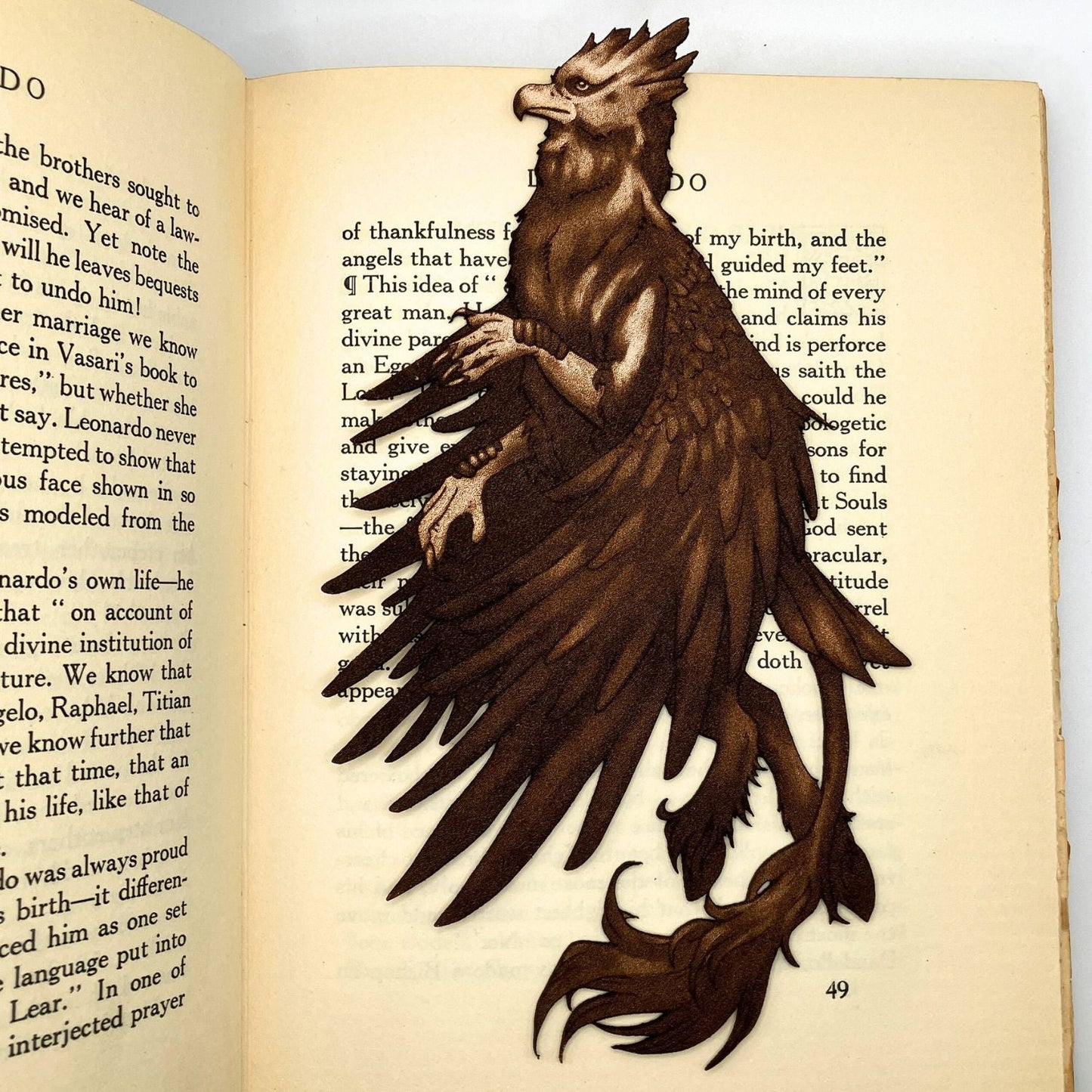 A leather hippogriff bookmark resting on the pages of a book. Leather Hippogriff Bookmark Bookmarks Raven King Crafts