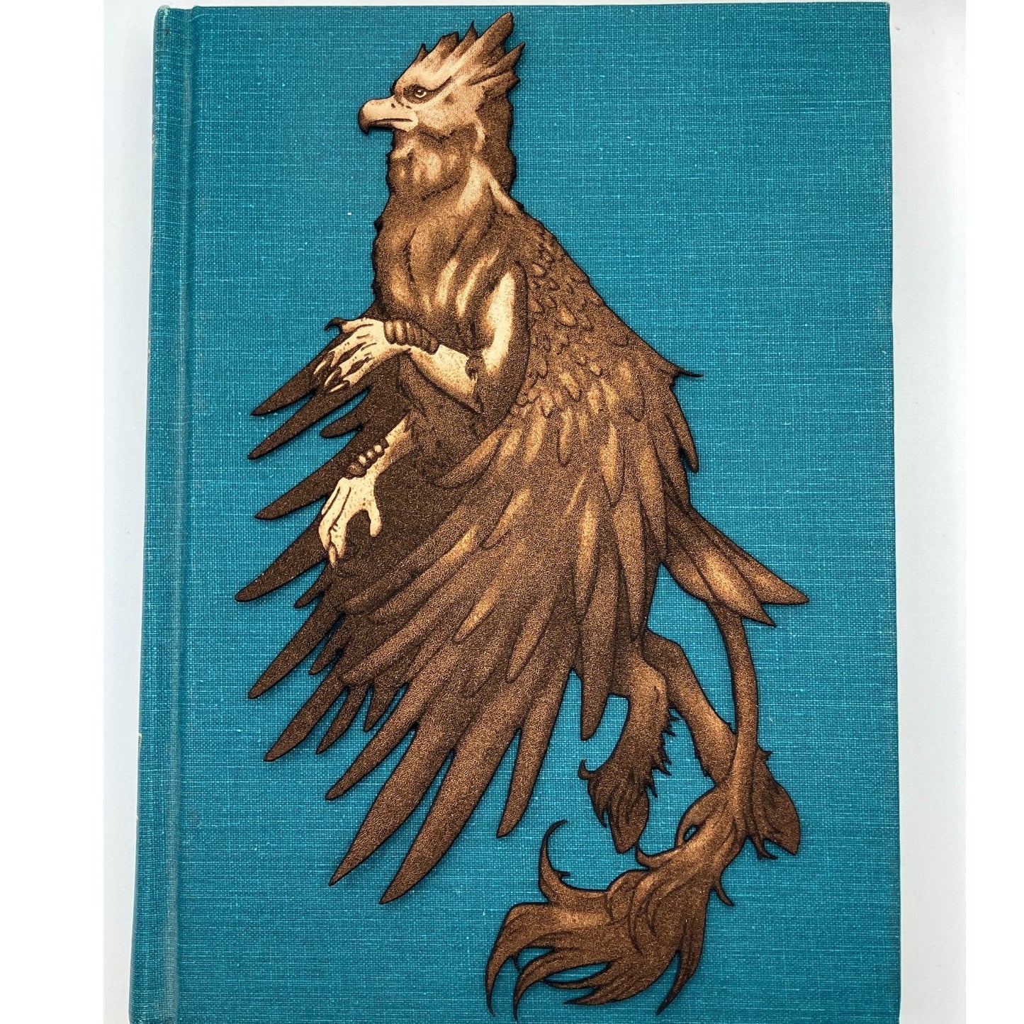 The leather hippogriff bookmark resting on the blue cover of a closed book. Leather Hippogriff Bookmark Bookmarks Raven King Crafts
