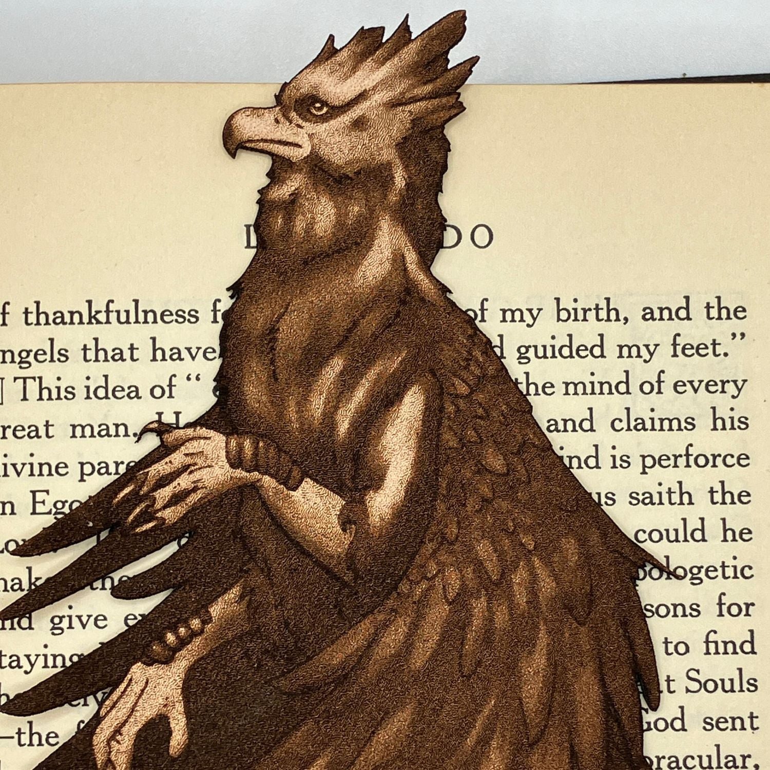 A leather hippogriff bookmark resting on the pages of a book. Leather Hippogriff Bookmark Bookmarks Raven King Crafts