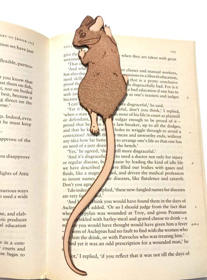 A photograph of exclusive climbing mouse leather bookmark resting on the pages of an open book. Leather Mouse Bookmark - Cute Little Book Buddy Bookmarks Raven King Crafts