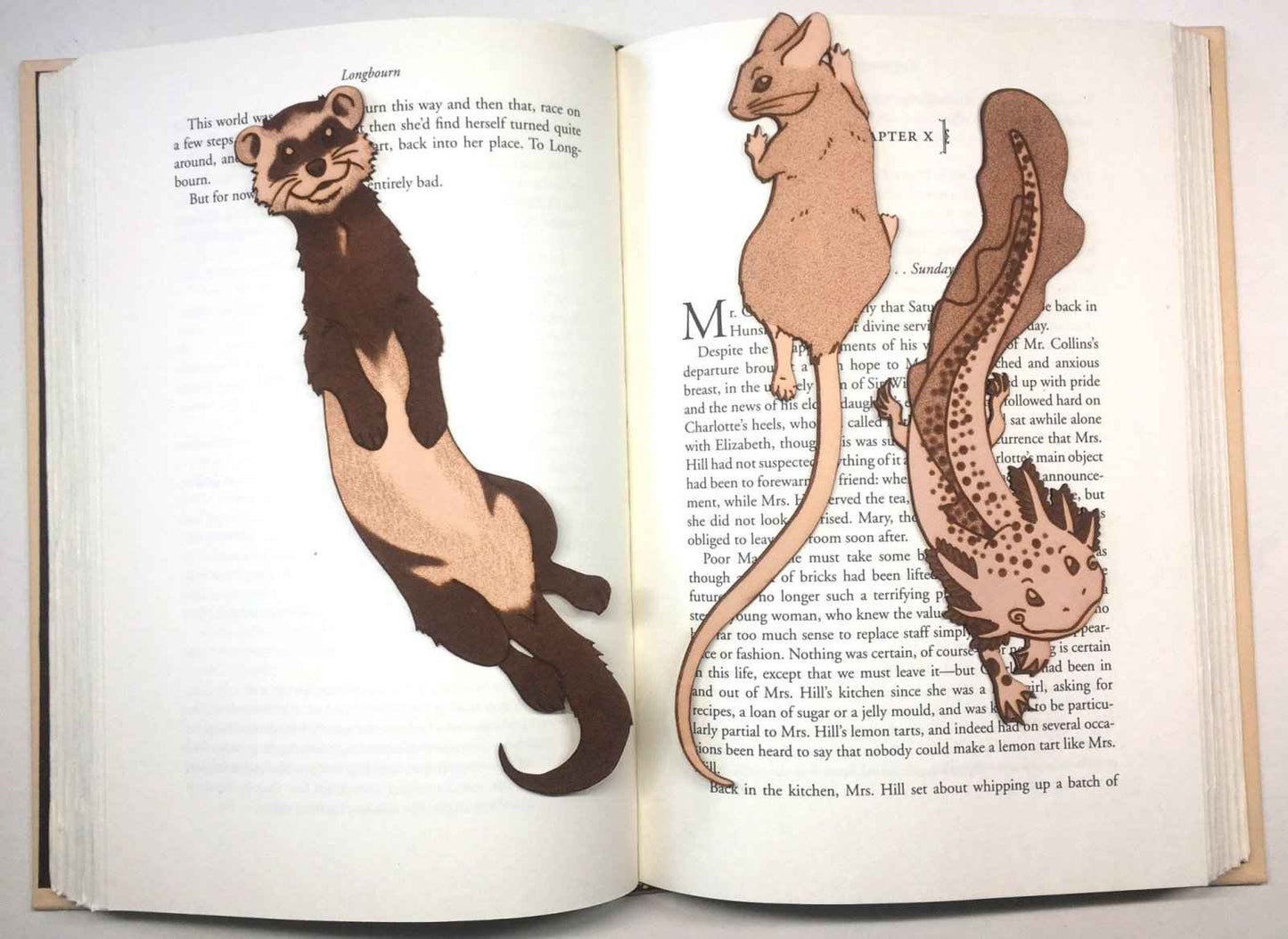 A photograph of exclusive climbing mouse leather bookmark resting on the pages of an open book. Leather Mouse Bookmark - Cute Little Book Buddy Bookmarks Raven King Crafts