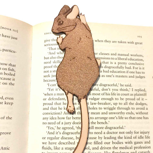 A photograph of exclusive climbing mouse leather bookmark resting on the pages of an open book. Leather Mouse Bookmark - Cute Little Book Buddy Bookmarks Raven King Crafts