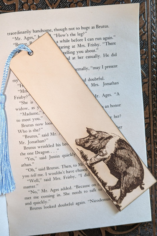 A leather bookmark of a hog with a white band, resting on the pages of an open book. Leather Pig or Hog Bookmark Bookmarks Raven King Crafts Leather Pig or Hog Bookmark Bookmarks Raven King Crafts