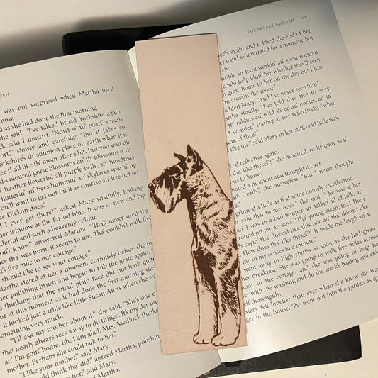 A leather rectangular shaped bookmark with the art of a Schnauzer engraved on it.