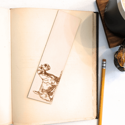The leather Sealyham, dog bookmark resting on the pages of an open book. to the right of it is a pencil and a glass for scale. Leather Sealyham Terrier Bookmark (toy dog) Bookmarks Raven King Crafts Leather Sealyham Terrier Bookmark (toy dog) Bookmarks Raven King Crafts