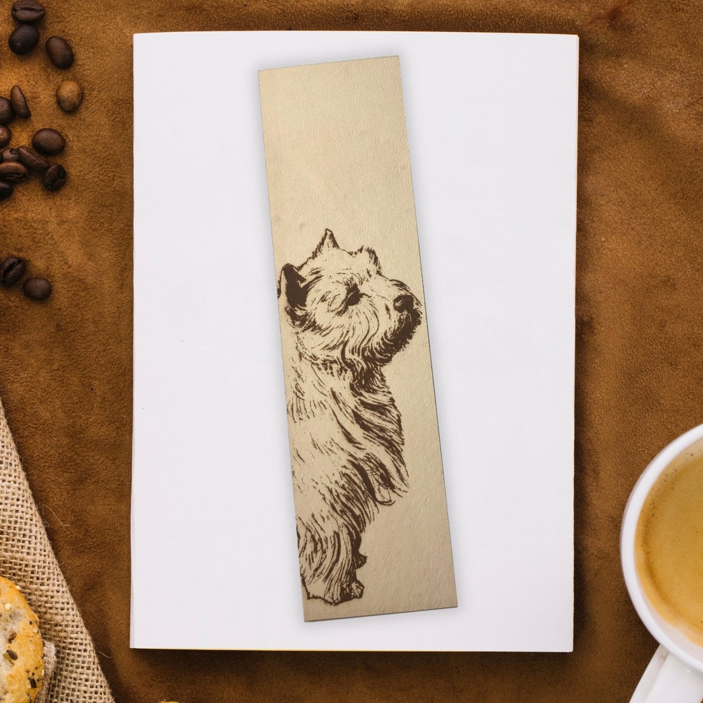 A bookmark with the art of a Westie engraved on it. The bookmark is on top of a closed book.