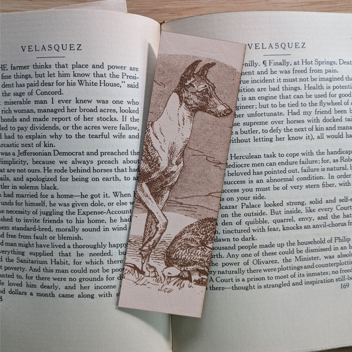 A rectangular leather bookmark with the historical art of a Whippet dog engraved on it. The bookmark is resting on the pages of an open book. Leather Whippet Dog Bookmark Bookmarks Raven King Crafts Leather Whippet Dog Bookmark Bookmarks Raven King Crafts