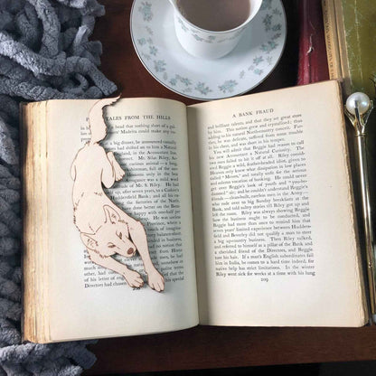 This leather wolf shaped bookmark is resting on the pages of an open book. Leather Wolf Bookmark - Unique Book Guardian for Book Lovers Bookmarks Raven King Crafts