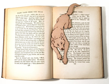 The leather bookmark shaped like a wolf leaping resting on an open book.