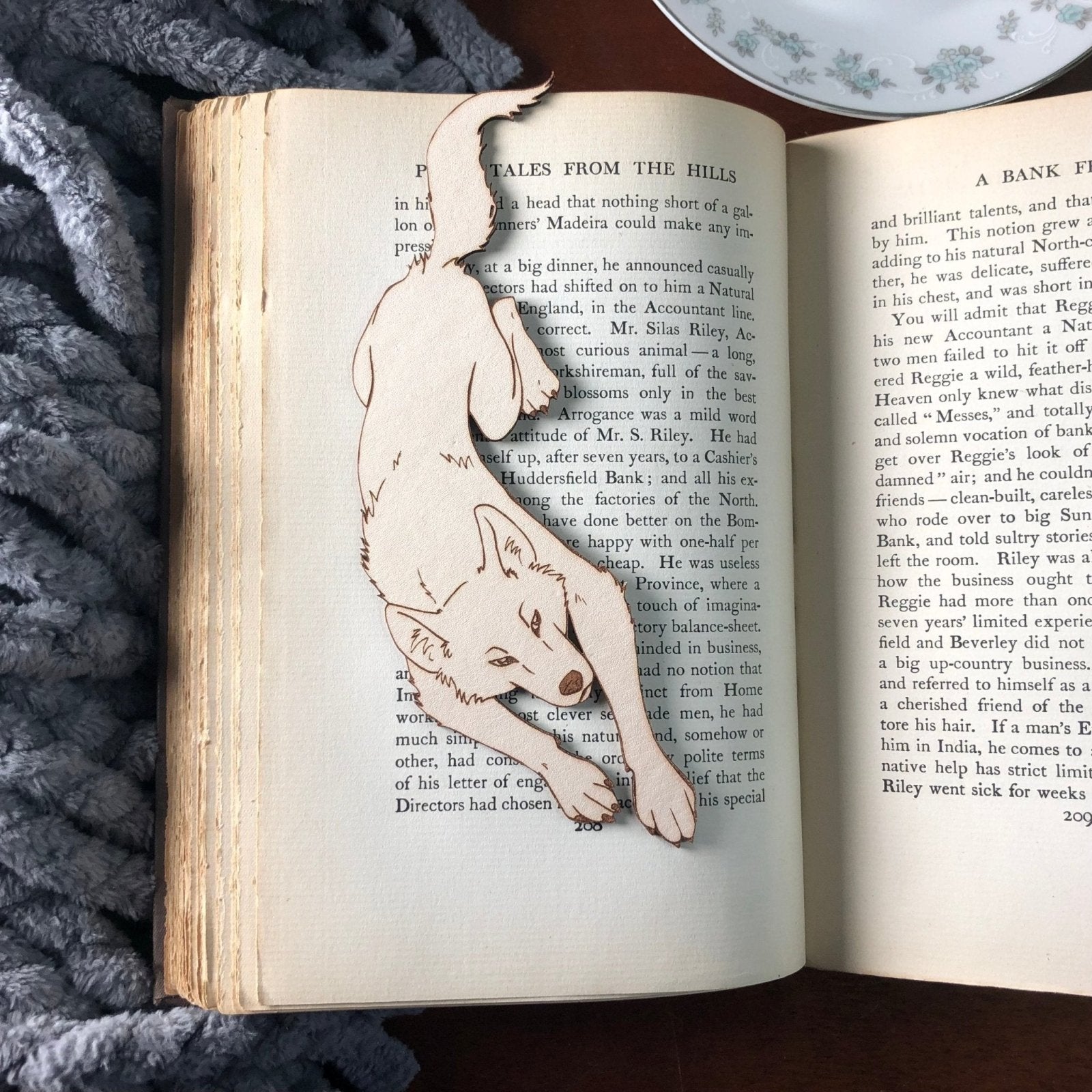 A leather bookmark made in the shape of a leaping wolf. The wolf is resting on an antique book.