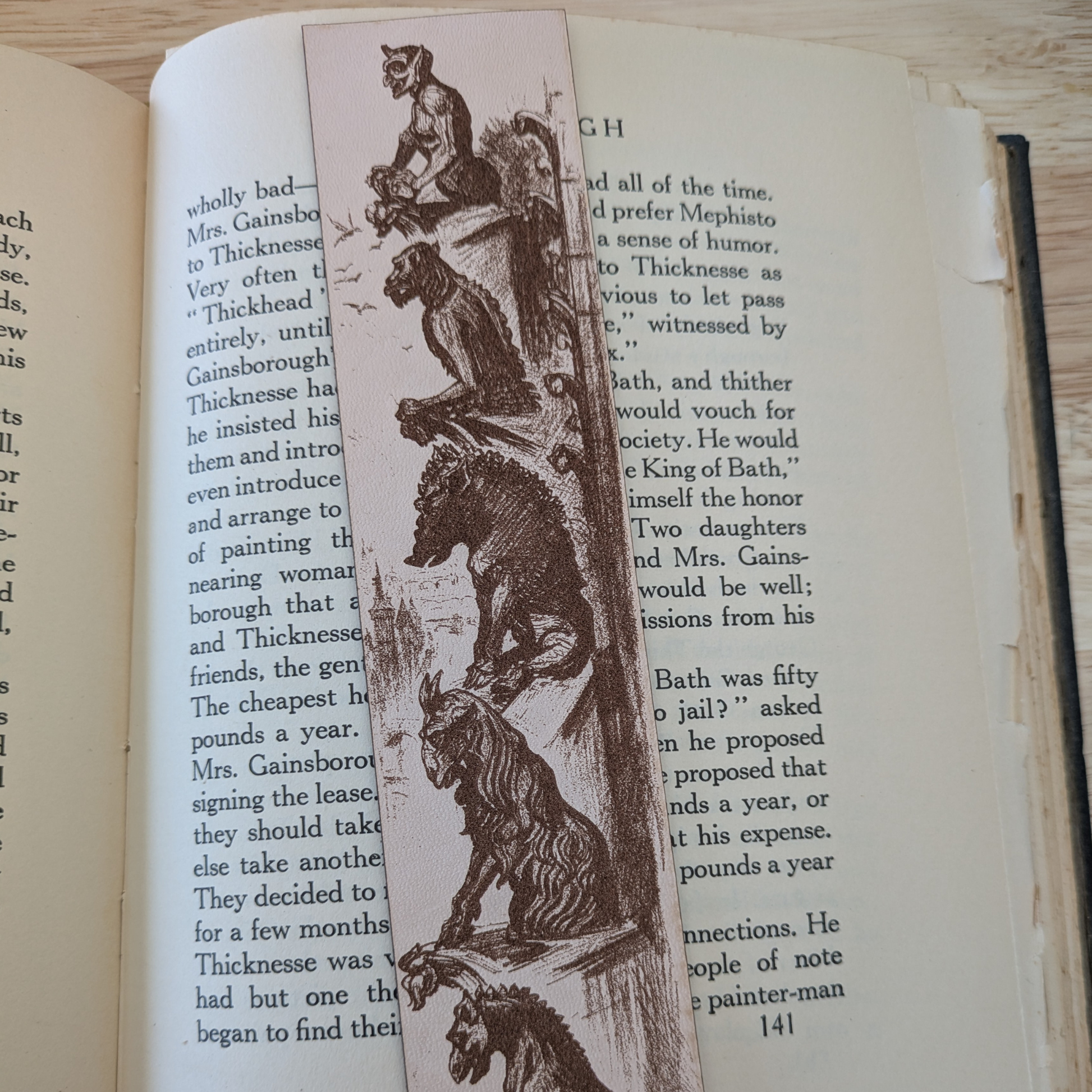 A leather bookmark engraved with the historical art of a collection of gargoyles. 