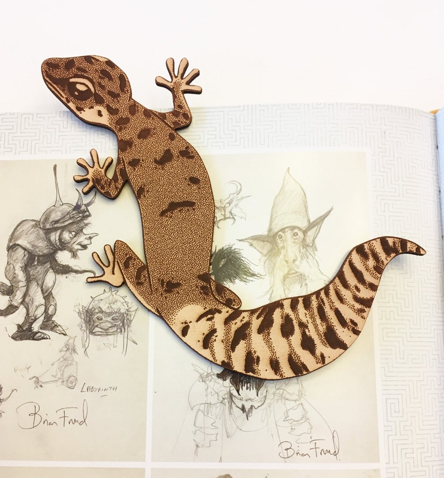 A leather bookmark shaped like a leopard gecko. The bookmark is sitting on an open book.