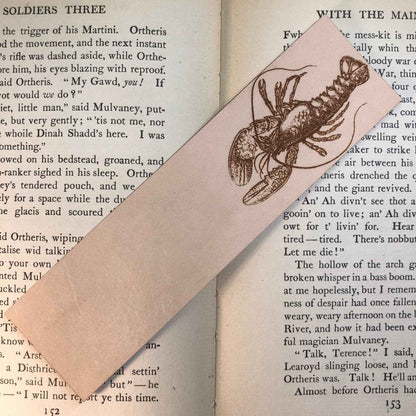 A photograph of historical lobster leather bookmark resting on the pages of an open book. Lobster Bookmark Bookmarks Raven King Crafts