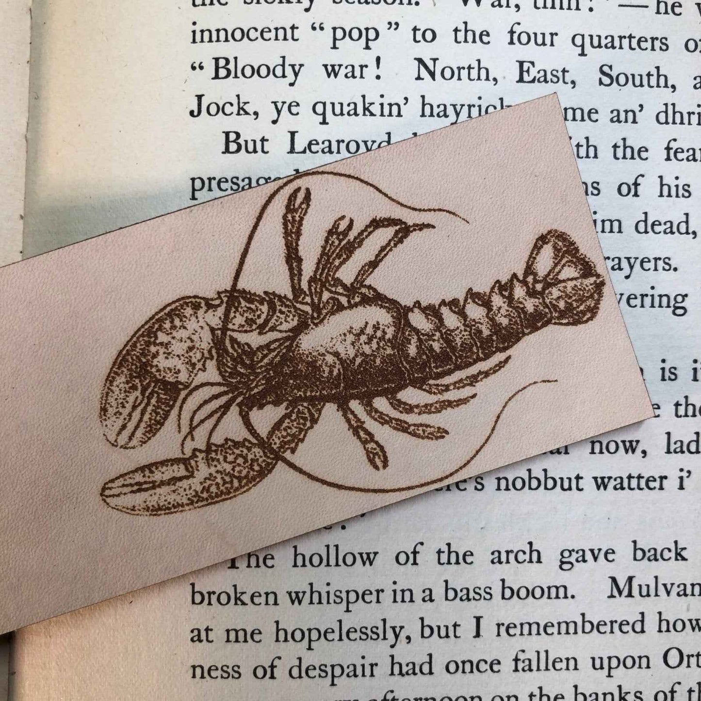 A photograph of historical lobster leather bookmark resting on the pages of an open book. Lobster Bookmark Bookmarks Raven King Crafts