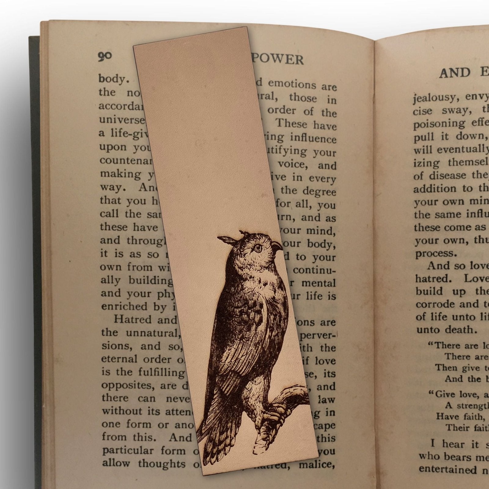 A leather bookmark with the art of a cat owl engraved on it. The bookmark is sitting on the pages of an open book. Long-eared Owl Bookmark - Leather Bookmarks Raven King Crafts