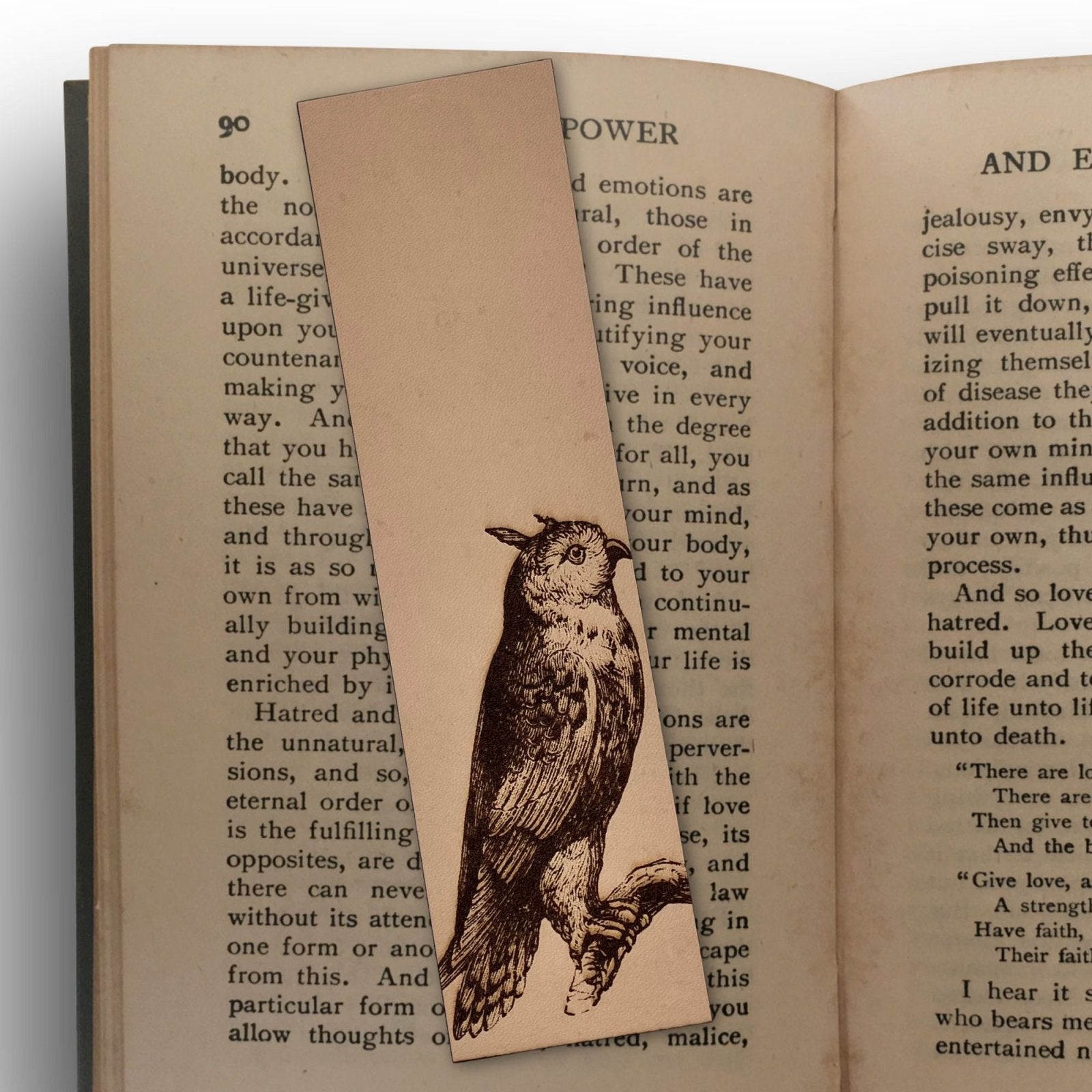 A leather bookmark with the art of a cat owl engraved on it. The bookmark is sitting on the pages of an open book.