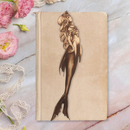 A mermaid shaped leather bookmark resting on a closed tan book.