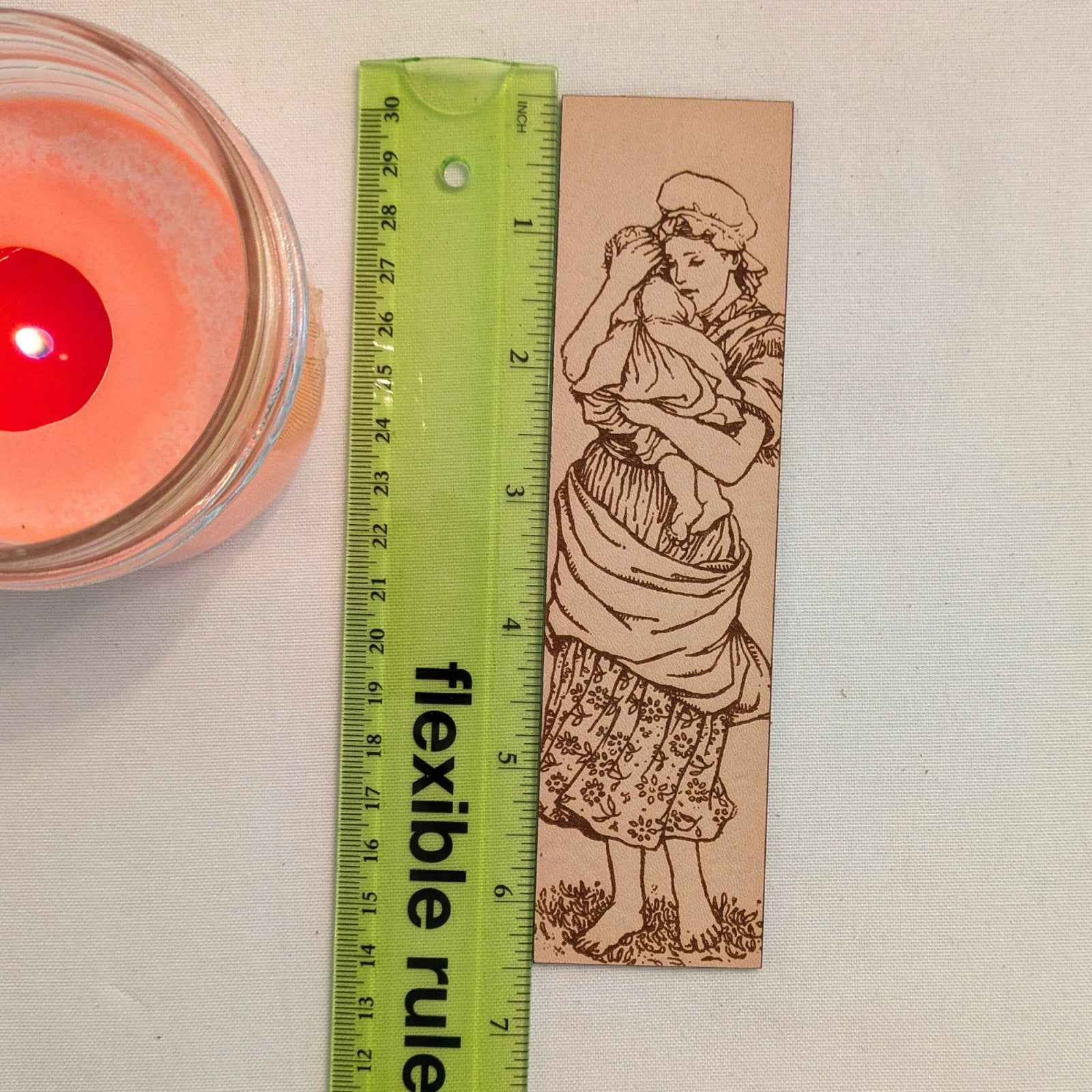 A photograph of historical mother holding a child leather bookmark next to a ruler for scale. Mother and Child Leather Bookmark Bookmarks Raven King Crafts