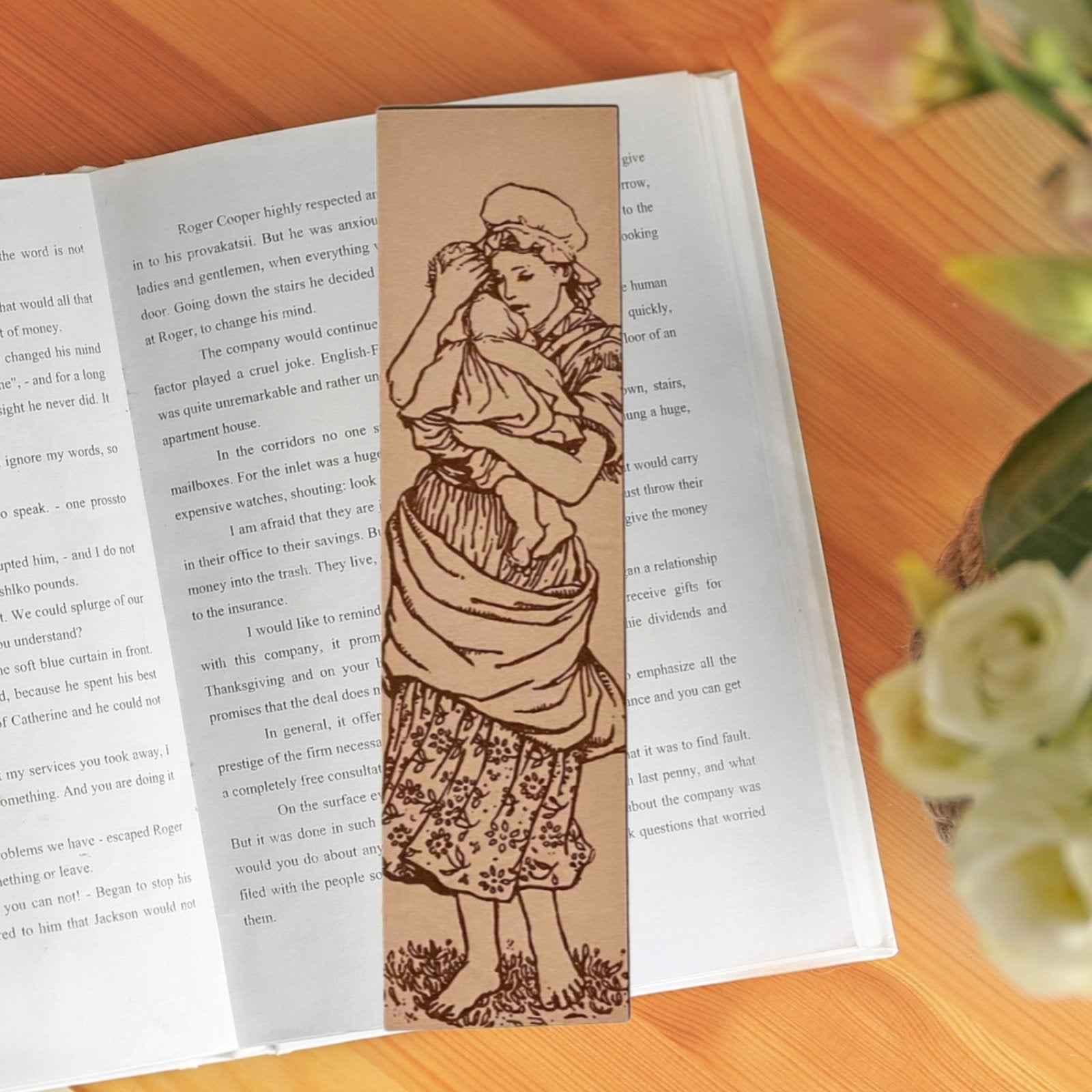 A photograph of historical mother holding a child leather bookmark resting on the pages of an open book. Mother and Child Leather Bookmark Bookmarks Raven King Crafts