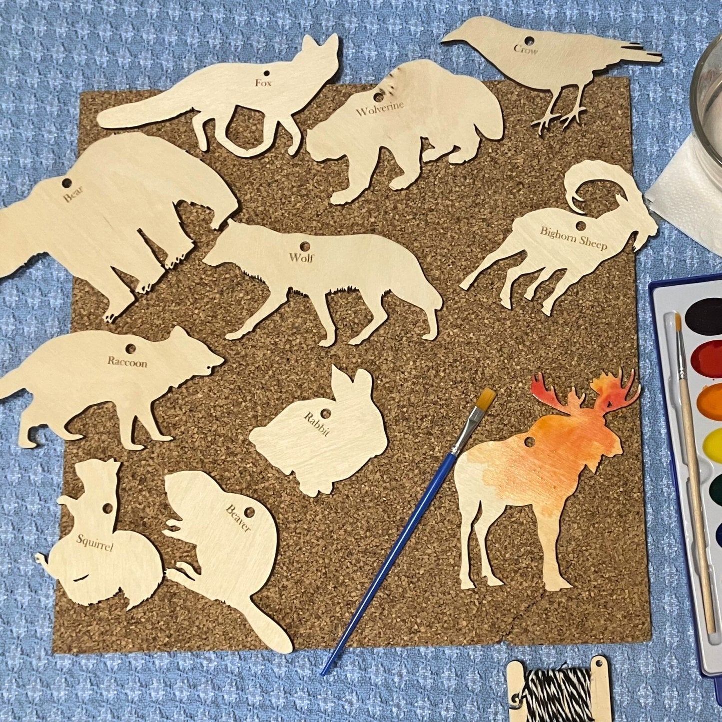 A collection of wood animal cutouts. The moose is being painted with watercolors.