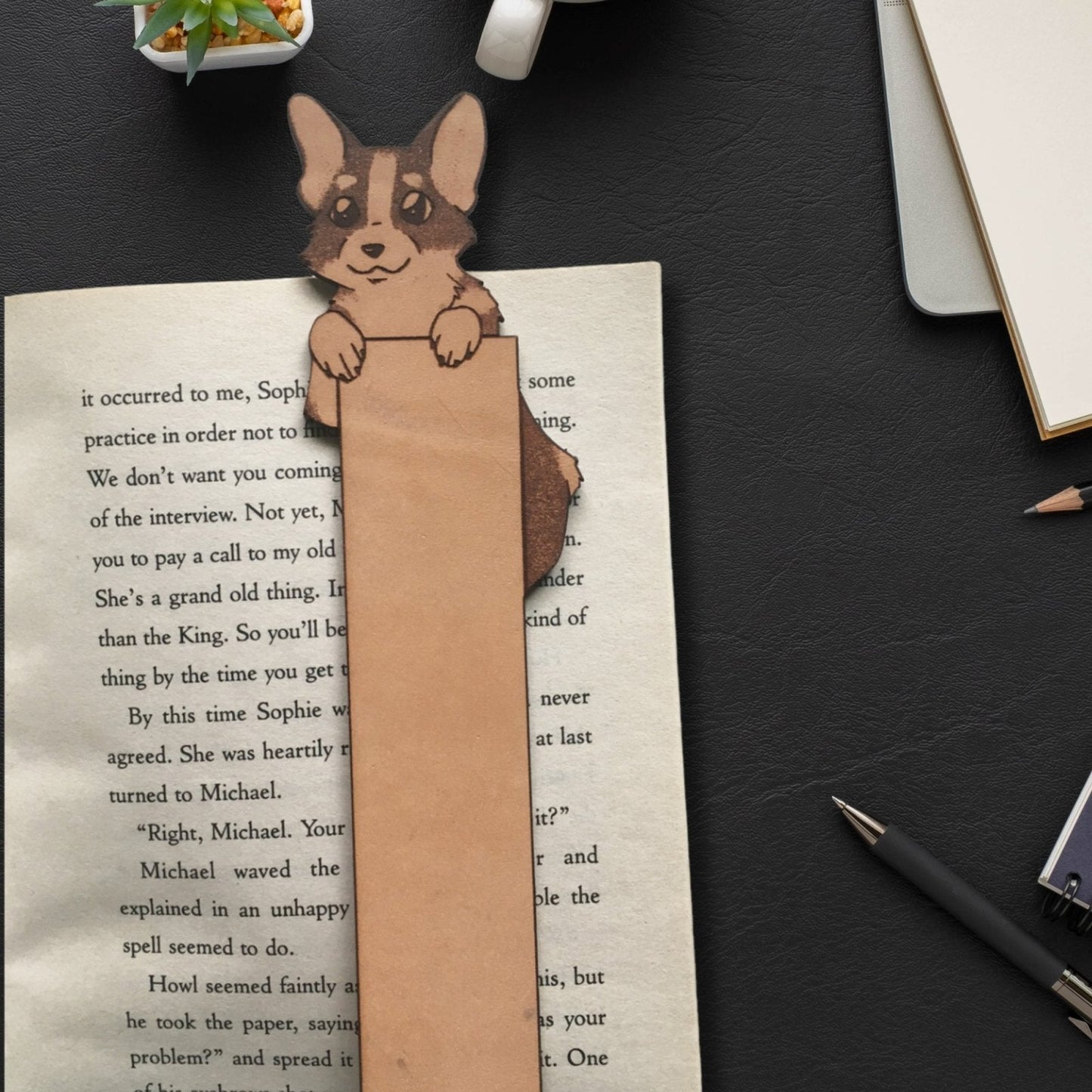 A photograph of a leather bookmark with a little corgi peeking over the top.