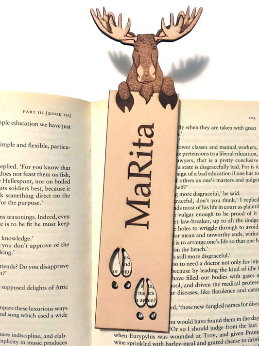 A photograph of exclusive personalizable moose leather bookmark resting on the pages of an open book. Personalizable Moose Leather Bookmark - Unique Gift for Book Lovers Bookmarks Raven King Crafts