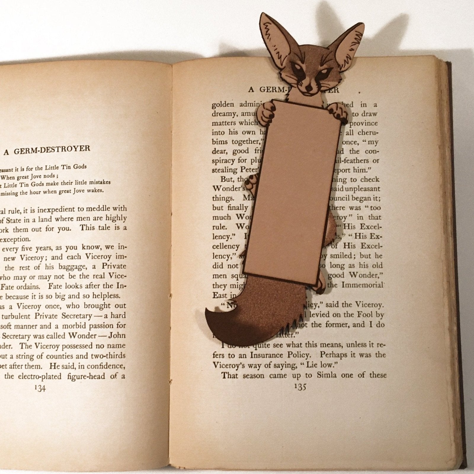 The photo shows a leather bookmark of a fennec fox holding a rectangular text area box.