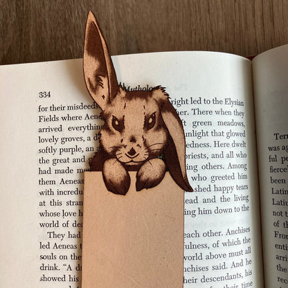 A photo of a bunny with one ear up and one down peeking over the top of the bookmark. Rabbit Bookmark - Leather Bookmarks Raven King Crafts
