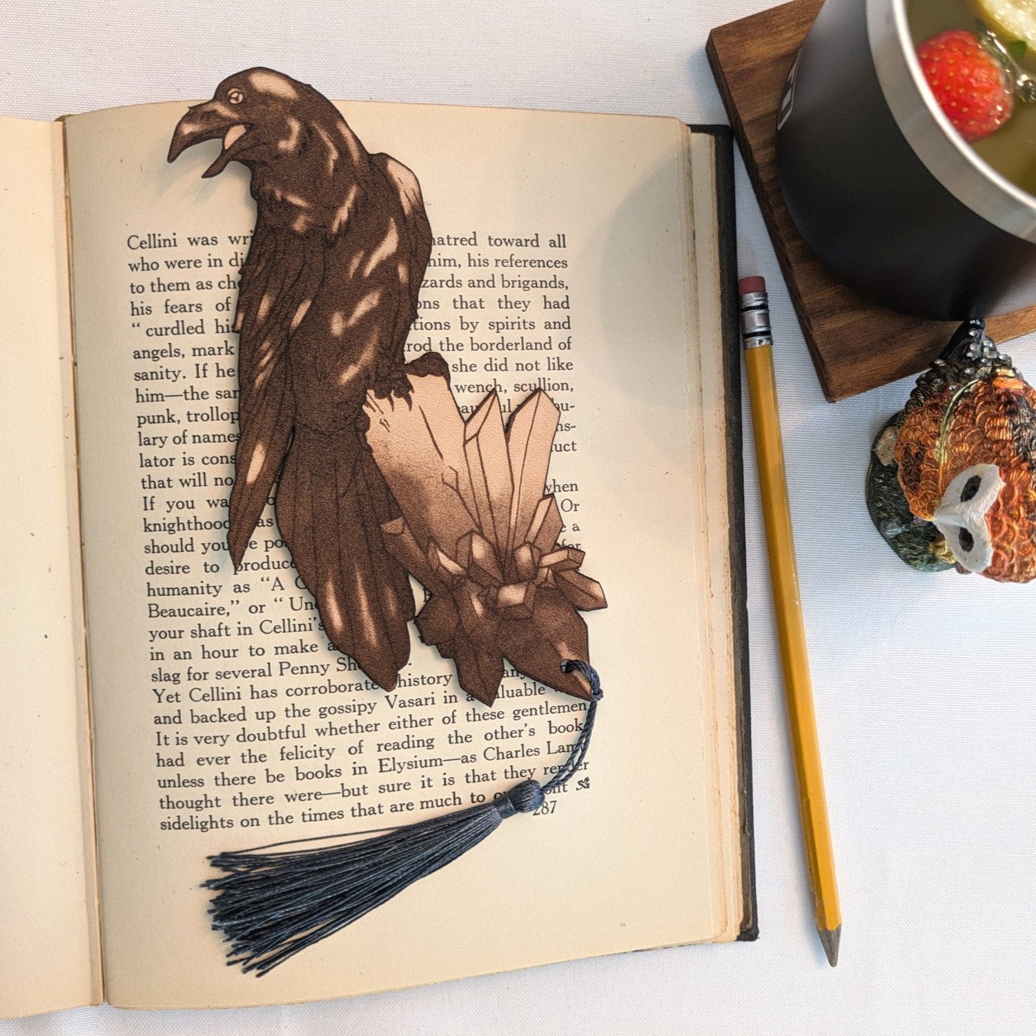 A photograph of exclusive raven on a crystal leather bookmark resting on the pages of an open book. Raven Bookmark - Leather Bookmarks Raven King Crafts