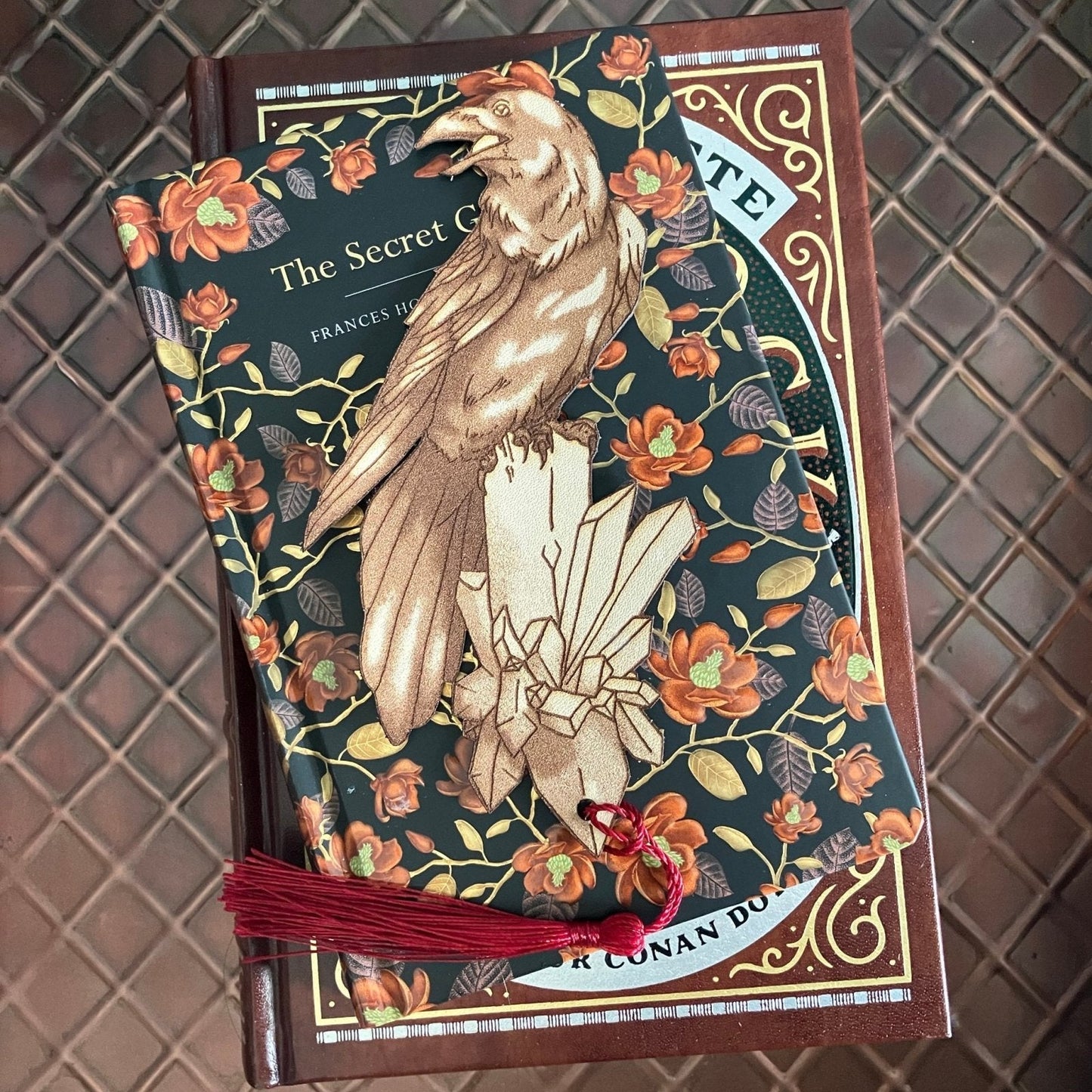 A leather raven shaped bookmark resting on some books. Raven Bookmark - Leather Bookmarks Raven King Crafts