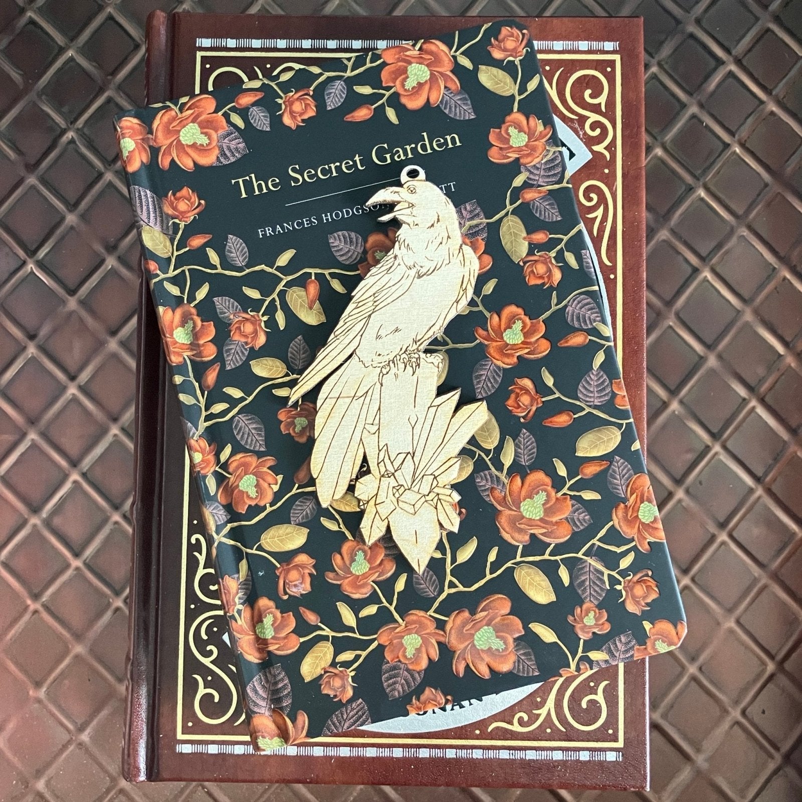 The raven ornament blank sitting on top of a stack of books. The raven ornament is a pale wood color. Raven with a Crystal Shaped Wooden Ornaments Art & Craft Kits Raven King Crafts