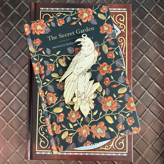 The raven ornament blank sitting on top of a stack of books. The raven ornament is a pale wood color. Raven with a Crystal Shaped Wooden Ornaments Art & Craft Kits Raven King Crafts