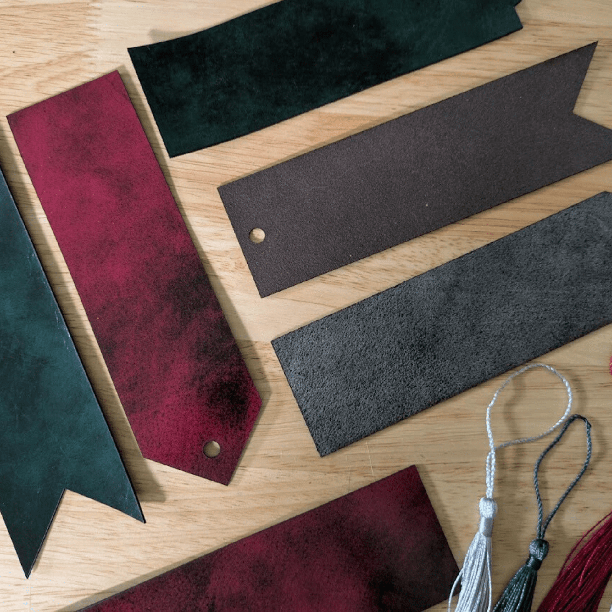A photograph of the green and red black dyed leather bookmarks. Top left is ribbon style green and black, red and black pointed, green rounded, red ribbon, green pointed, red rounded and the tassels. Red or Green Leather Bookmarks with Tassel Bookmarks Raven King Crafts