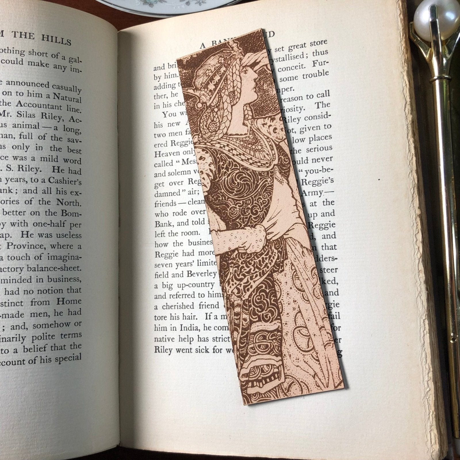 A leather bookmark with the art of a queen or princess looking out. She has braids, an ornate crown, and ornate robes.