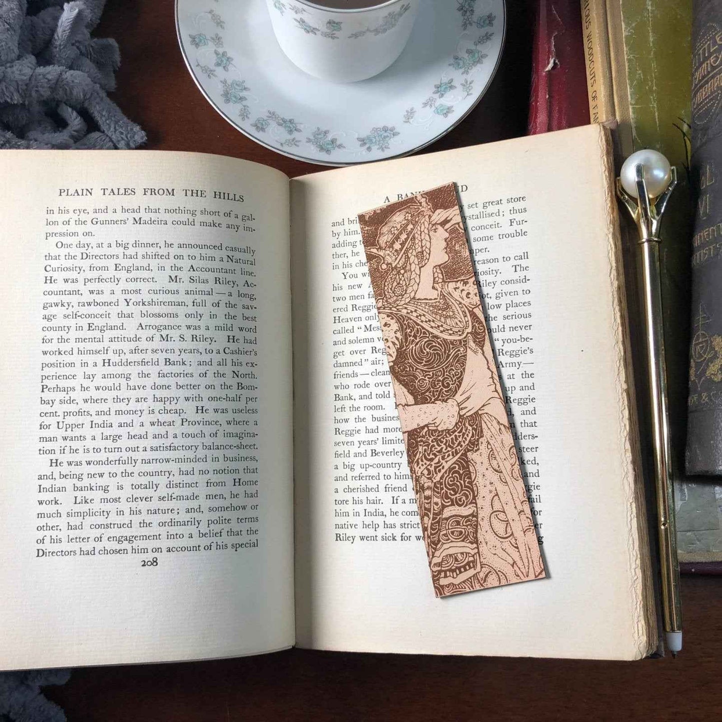 A leather bookmark with the antique art of a regal queen in a tower on it. The bookmark is resting on the pages of an open book. Regal Queen In Tower Leather Bookmark Bookmarks Raven King Crafts