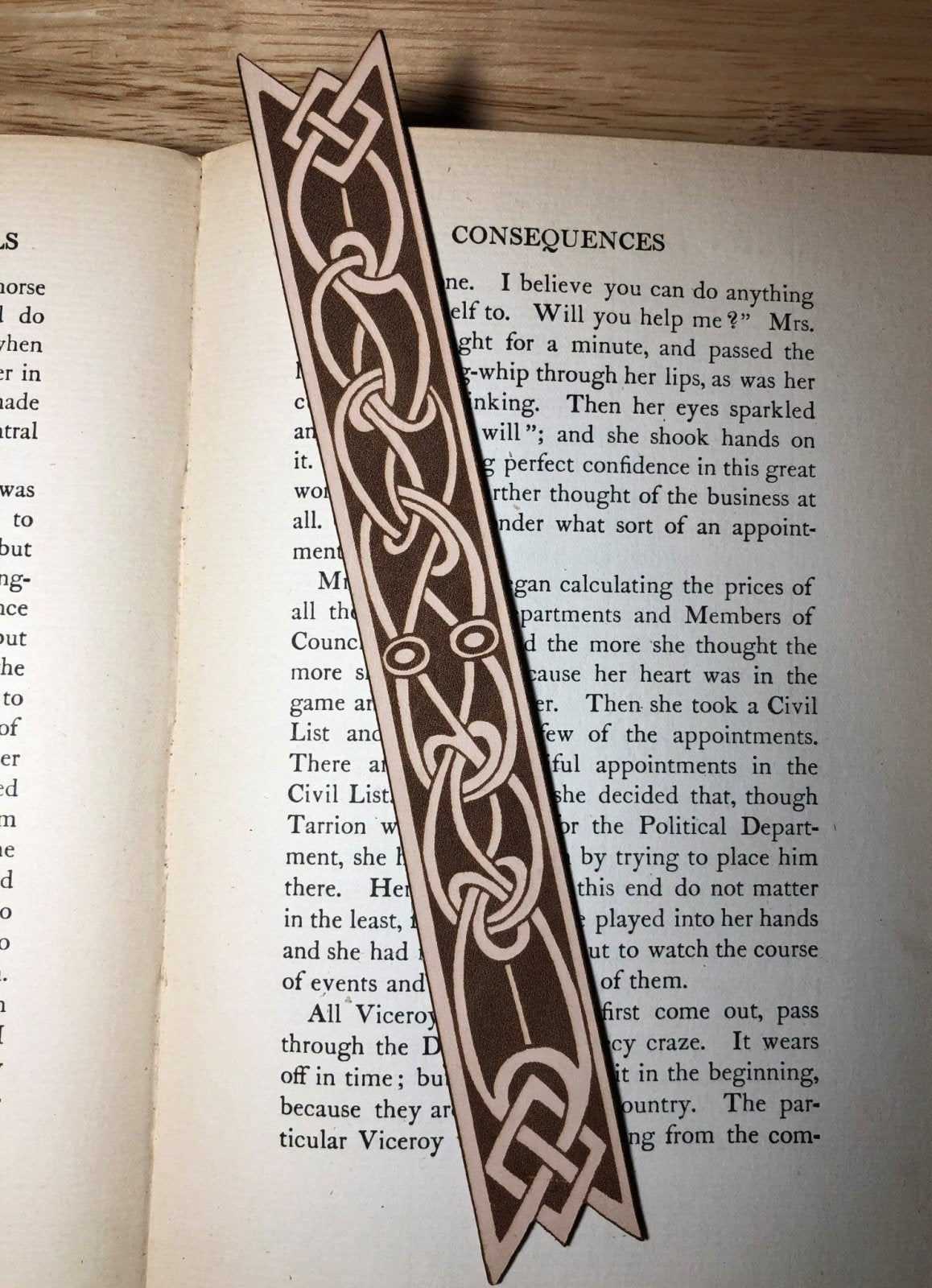 Another photograph of the Celtic knot bookmark shaped like a ribbon. The leather bookmark is on the pages of an antique book.