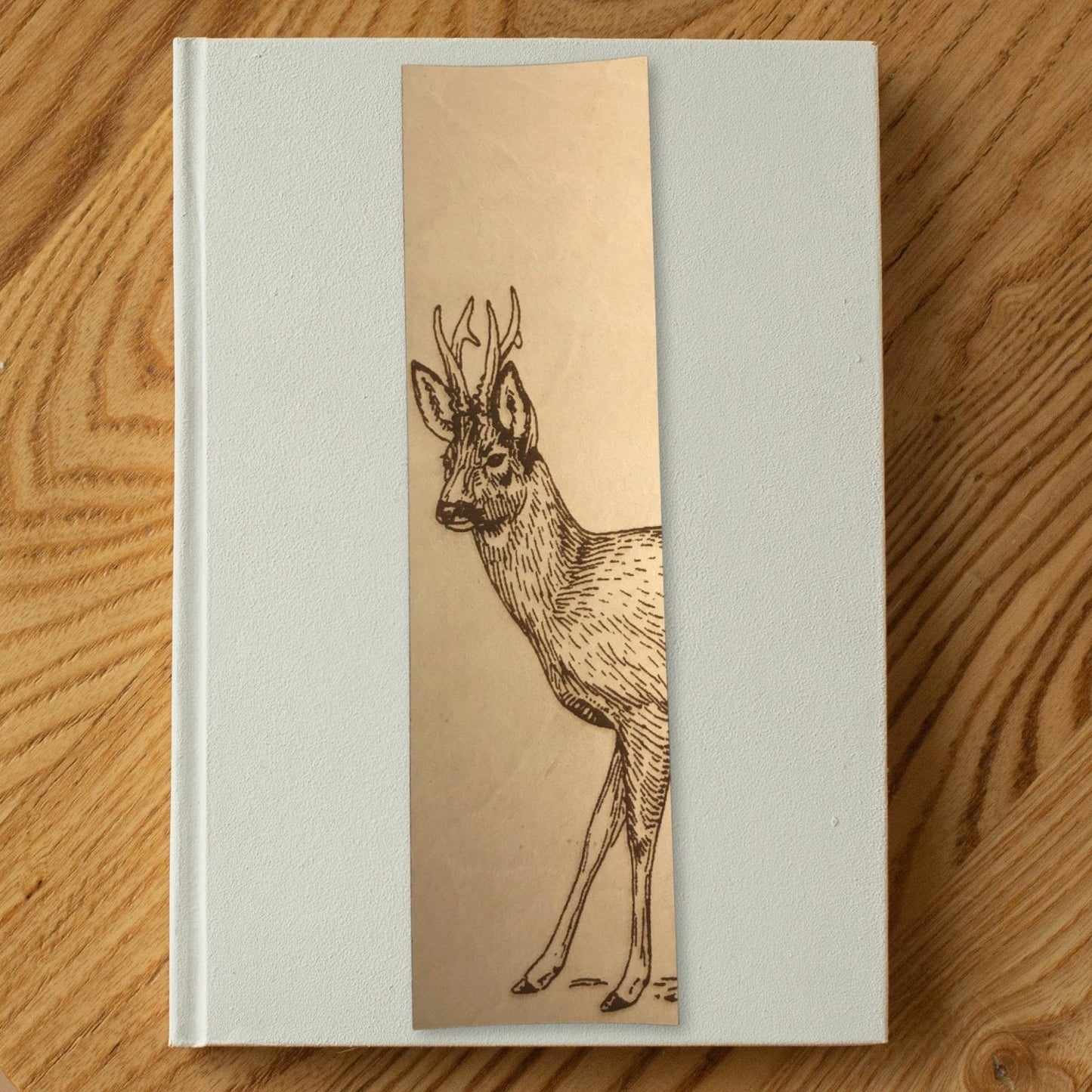 A photo of the roe deer bookmark resting on a white book. Roe Deer Bookmark - Leather Bookmarks Raven King Crafts