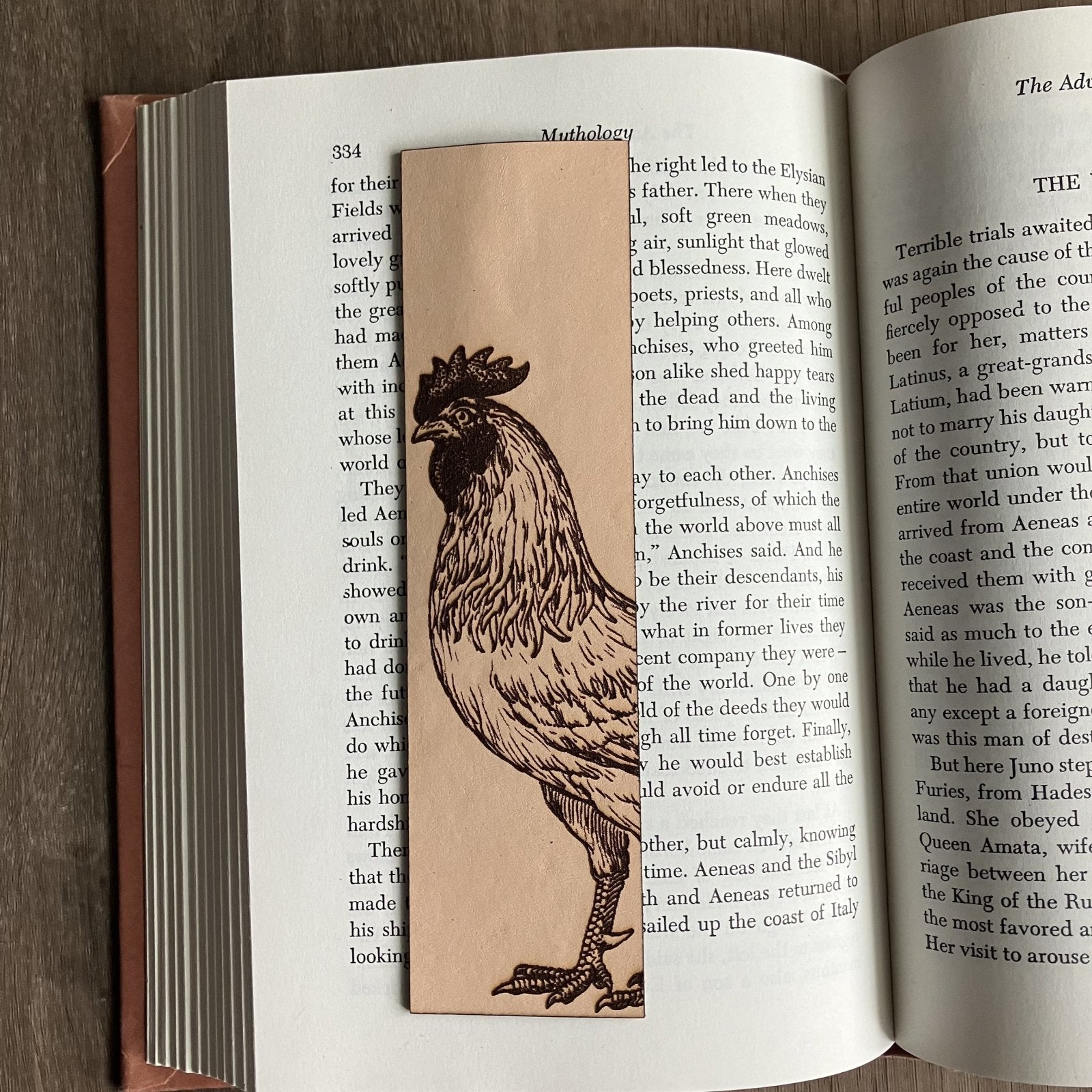 A rectangular bookmark with the art of a rooster engraved on it. The bookmark is resting on the pages of an open book. Rooster Bookmark - Leather Bookmarks Raven King Crafts