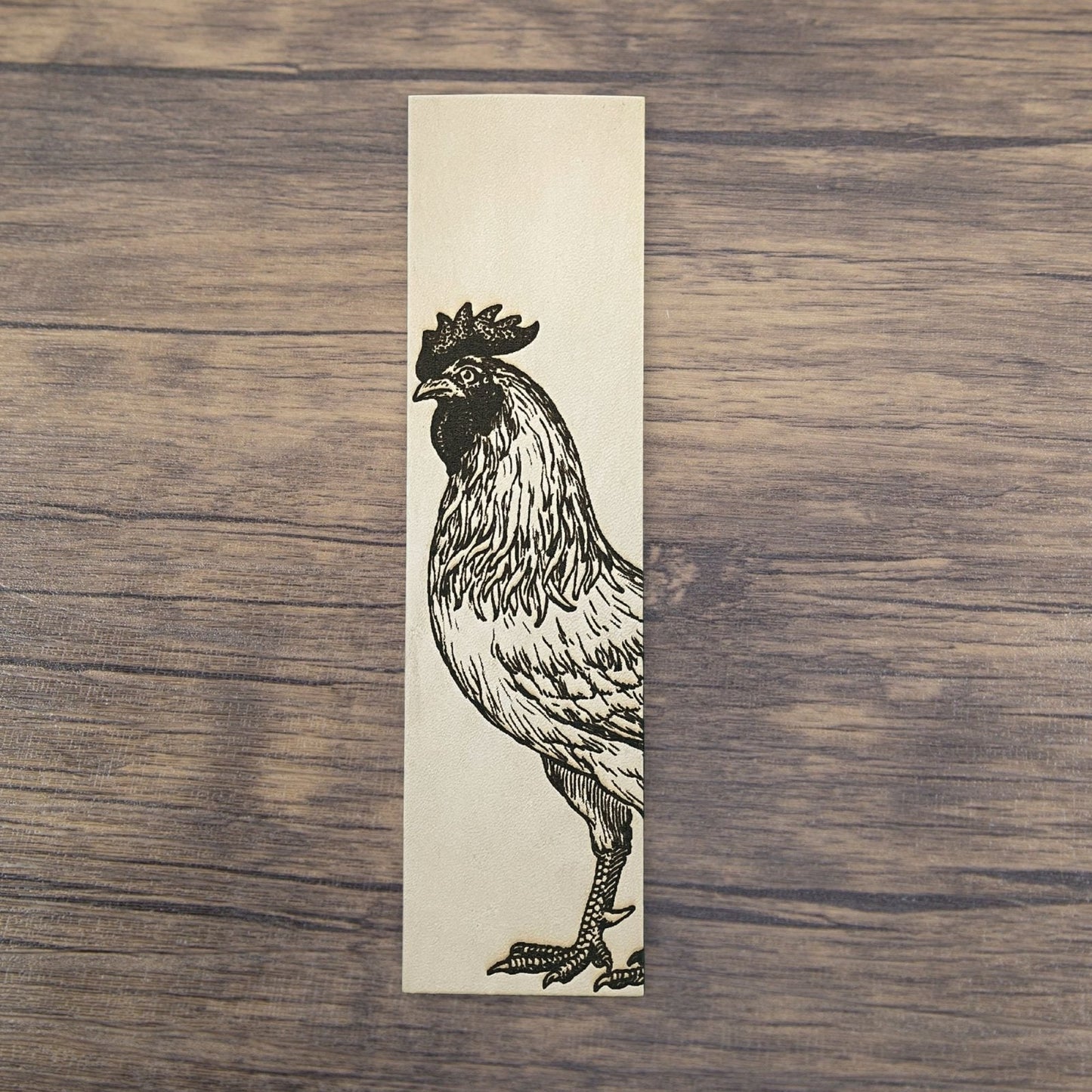 A rectangular bookmark with the art of a rooster engraved on it.