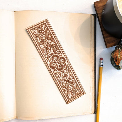A photograph of historical rounded cross medallion leather bookmark resting on the pages of an open book. Rounded Cross Medallion Bookmark Bookmarks Raven King Crafts