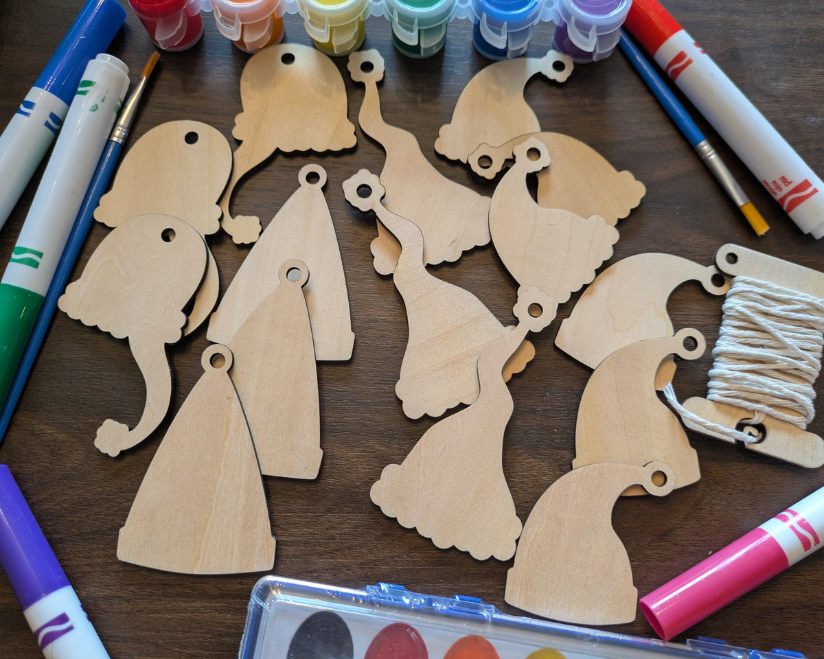A photograph of the wooden Santa hat Christmas ornament blanks. Around them are markers and paints you can select.