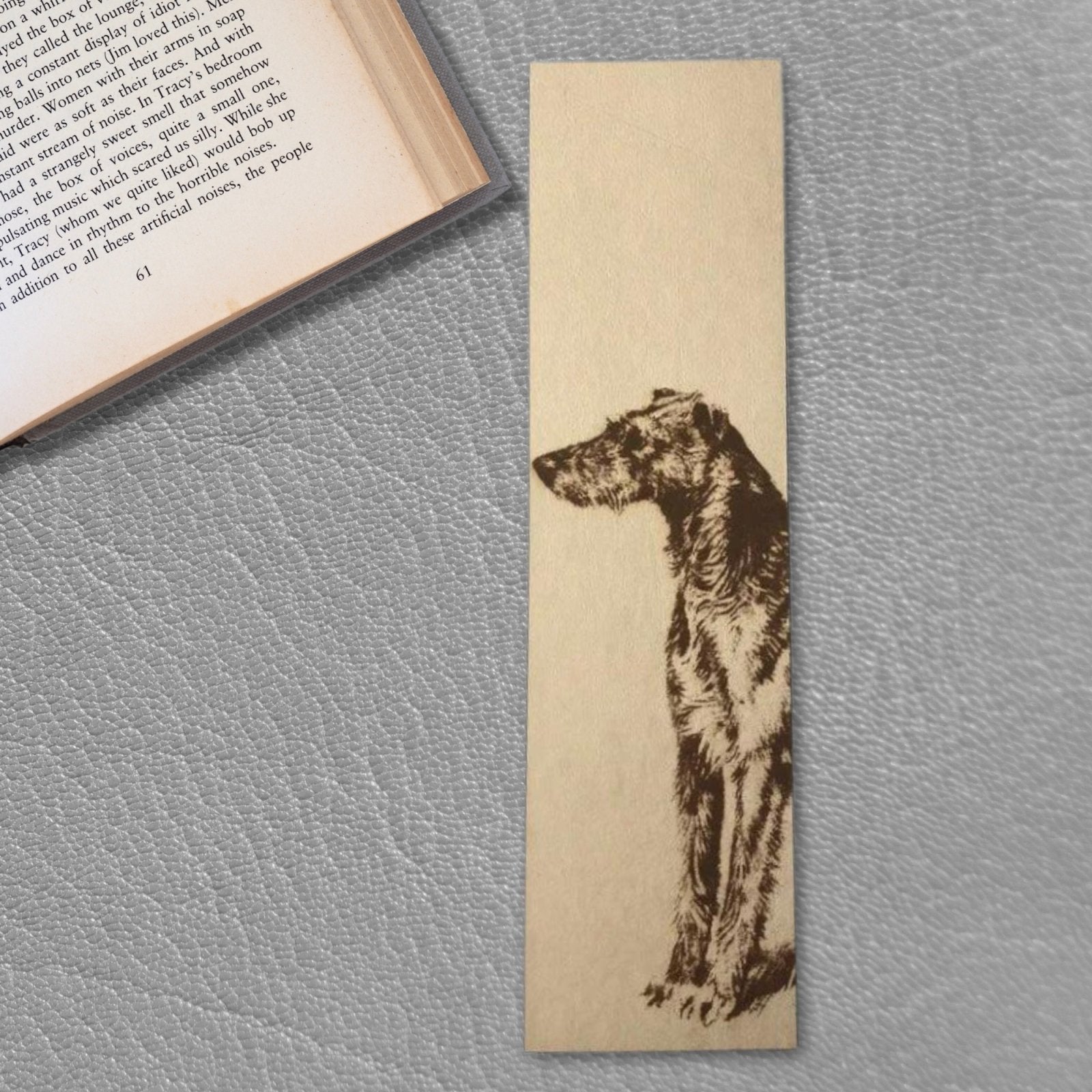 The leather Scottish Deerhound bookmark resting on a grey leather next to an open book.