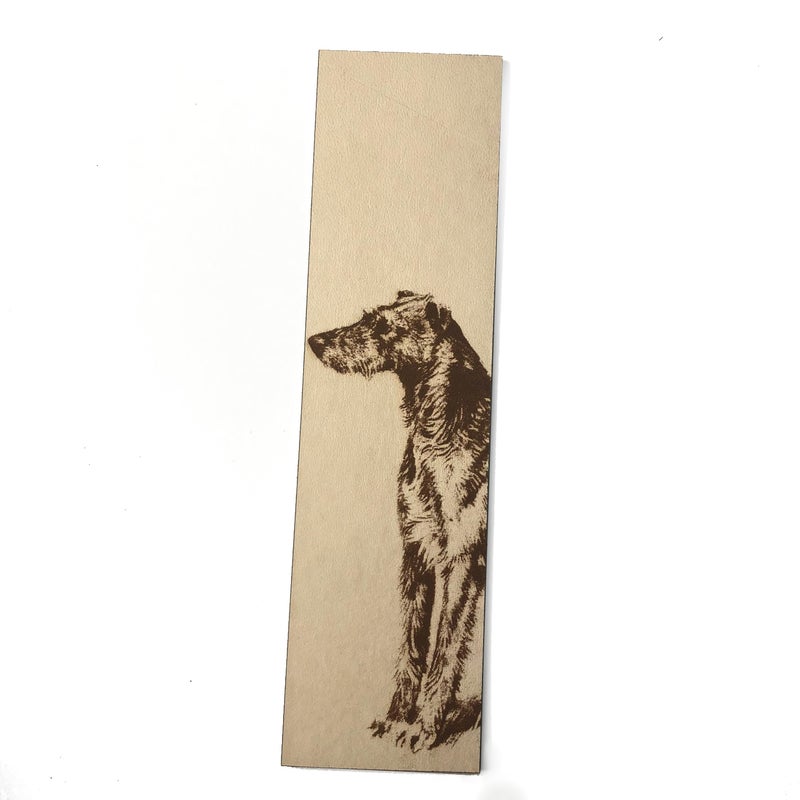 A leather rectangle shaped bookmark with the art of a dog engraved on it.