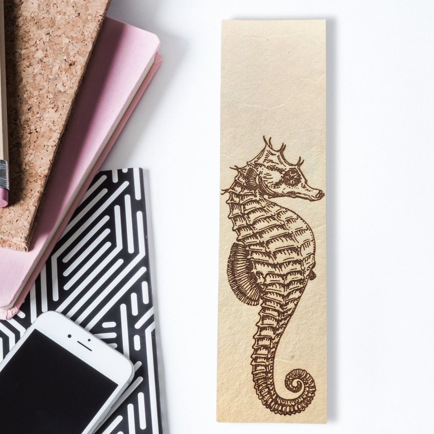 A leather seahorse bookmark next to some notepads and a cellphone.