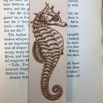 A close up of the engraved seahorse art on the bookmark. The bookmark is sitting on an antique book.