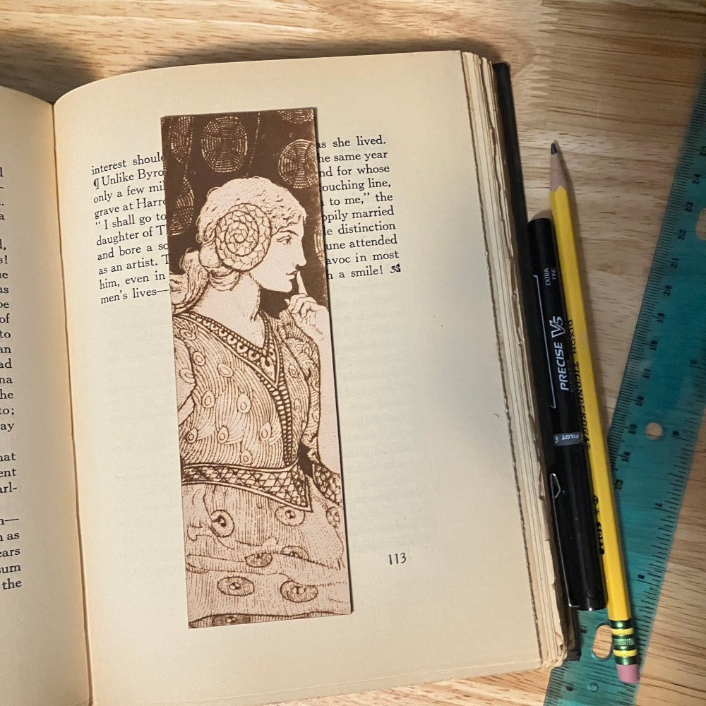 A leather bookmark with the art of a seated woman shushing someone. Shushing Woman Bookmark - Leather Bookmarks Raven King Crafts