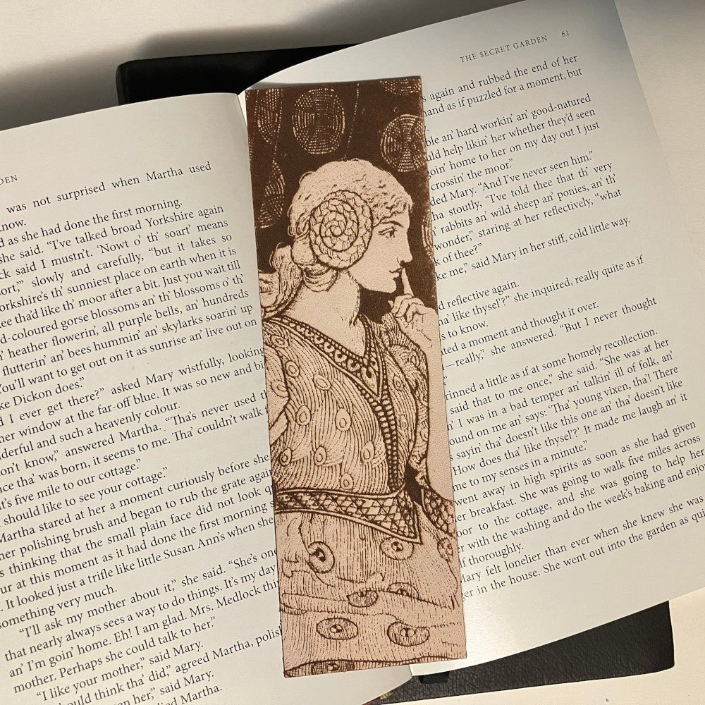 A leather bookmark with the art of a seated woman shushing someone.