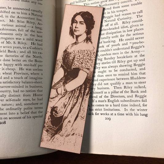 A photo of the leather bookmark resting on an antique book. The bookmark has the art of a woman engraved on it.